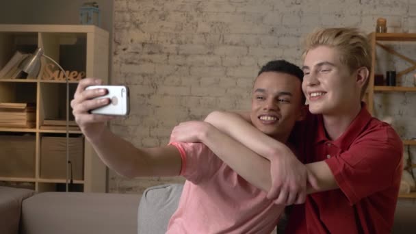 Sarılma, selfies yapma, gülüyor kanepede oturan iki uluslararası gay arkadaş. Homeliness, romantik akşam, arka plan, hugs, mutlu Lgbt aile kavramı. 60 fps — Stok video