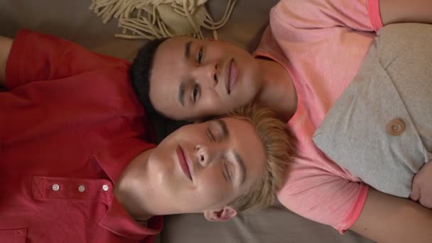 Международная гей-пара лежит на диване. Гомосексуализм, ЛГБТ-ловер Счастливая семейная концепция. Топ выстрел 60 кадров в секунду — стоковое видео