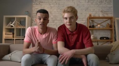 İki gay çocuklar kanepede oturan ve tarassut Tv, duygu beklenti ve sevinirler, gülme. LGBT aşıklar, mutlu bir eşcinsel aile ev rahatlık kavramı. Bak fotoğraf makinesi vasıl 60 fps
