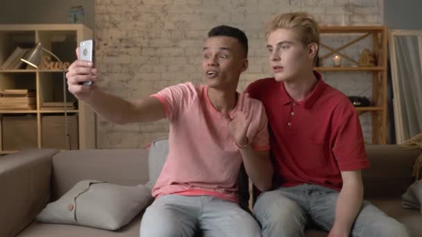 Two Multi Ethnic Homosexual Friend Sitting On The Couch Embracing And Showing A Greeting Gesture In A Video Chat Happy Lgbt Couple Concept Gay Lovers 60 Fps