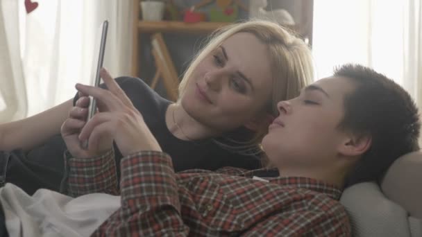 Лесбиянская пара отдыхает на диване, используя планшетный компьютер, прокручивая фотографии на планшете, семейная жизнь, любовь, симпатичная, крупным планом 60 кадров в секунду — стоковое видео