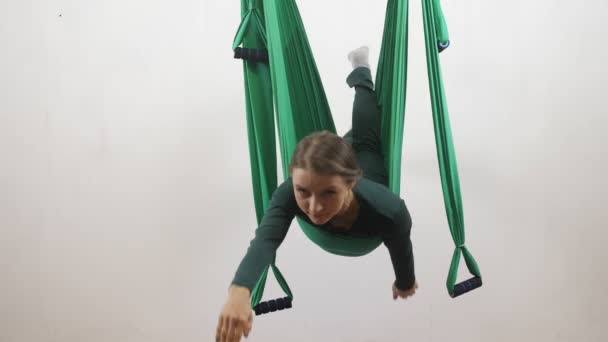 Молода біла жінка робить антигравітаційні вправи мухами йоги в гамаку в студії в приміщенні. Повітряний аеродинамічний тренажер тренування літаків. Супермен позує, медитує, гармонія і концепція спокою 60 кадрів в секунду — стокове відео