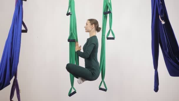 Mladá Kavkazský žena dělat antigravitační fly jóga cvičení v houpací síti ve studiu doma. Letecká aero překrýt fitness trenér cvičení. Lotus pose, medituje, harmonii a vyrovnanosti koncept, boční pohled 60 fps