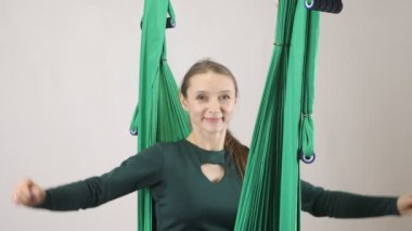 Üzerinde bir hamak gülümseyen genç kadın oturur sevinir ve ellerini yukarı yükseltir. Hava aero sinek fitness eğitmeni egzersiz. Meditasyon, uyum ve huzur kavramı, 60 fps