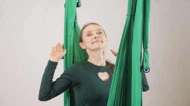 Genç kadın bir hamak streç eller gülümseyen ve yawing oturur. Hava aero sinek fitness eğitmeni egzersiz. Meditasyon, uyum ve huzur kavramı, 60 fps