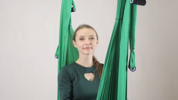 Junge Frau sitzt lächelnd auf einer Hängematte und sendet einen Luftkuss. aerial aero fly Fitness-Trainer-Workout. meditiert, Harmonie und Gelassenheit Konzept, 60 fps — Stockvideo