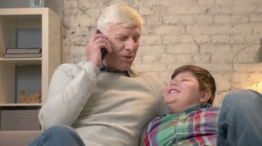 Dede ve torunu kanepede oturuyor. Yaşlı adam bir akıllı telefon telefonda konuşurken ve gülümseyen torunu seyir, elinde tutuyor. Ev konfor, iletişim, Aile İdil