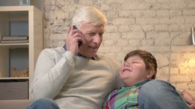 Dede ve torunu kanepede oturuyor. Yaşlı adam bir akıllı telefon elinde tutuyor, telefonda konuşuyor, torununa telefon verir. Ev konfor, iletişim, Aile İdil, rahatlık kavramı