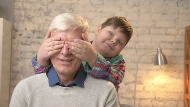 El niño gordo cierra los ojos de sus abuelos con las manos. Adivina quién. Un juego, una broma. El nieto mira a la cámara y hace caras graciosas. Concepto familiar feliz. 60 fps — Vídeos de Stock