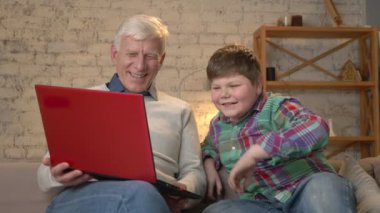 Dede ve torunu oturuyor kanepe ve laptop komik bir film izlerken, gülüyor üzerinde. Ev konfor, Aile İdil, rahatlık kavramı, nesillerin fark 60 fps
