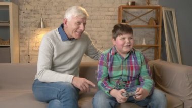 Torunu konsol oyunu oynar gibi büyükbaba saatler. Yaşlı adam genç bir şişman çocuk ile kanepede oturuyor. Video oyunu. Ev konfor, Aile İdil, rahatlık kavramı, farkı
