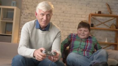 Dede torunu ile kanepede oturan video oyun konsolu çalış. Yaşlı bir adam kanepede oturuyor ve video oyunları oynarken oyun denetleyicisi tutar. Ev konfor, Aile İdil, rahatlık