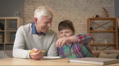 Dede torunu ev ödevlerinde yardımcı olur. Yaşlı adam genç bir şişman çocuk ev ödevi yapmak yardımcı olur. Ev konfor, Aile İdil, rahatlık kavramı, fark nesillerin, yakın çekim. 60 fps