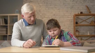 Dede torunu ev ödevlerinde yardımcı olur. Yaşlı adam genç bir şişman çocuk ev ödevi yapmak yardımcı olur. Ev konfor, Aile İdil, rahatlık kavramı, fark nesillerin, yakın çekim. 60 fps