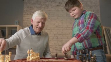 Dede ve torunu satranç oynamak hazırlanıyorlar. Yaşlı bir adam şişman bir çocuk satranç oynamasını öğretir. Satranç parçaları ortaya çıkarmak. Ev konfor, Aile İdil, rahatlık kavramı