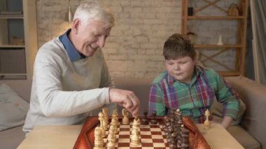 Dede ve torunu satranç oynar. Yaşlı adam genç bir şişman çocuk oynamak için satranç öğretir. Ev konfor, Aile İdil, rahatlık kavramı, fark nesillerin, yakın çekim. 60 fps