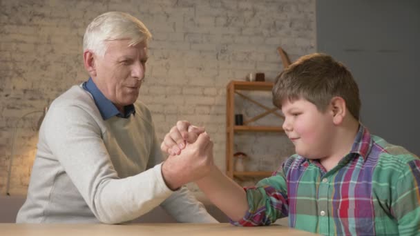 Opa en kleinzoon arm worstelen in een gezellige kamer thuis. Het meten van krachten in arm worstelen. Jong vet kind gewonnen. Home comfort familie idylle, gezelligheid concept, verschil van generaties, close-up — Stockvideo