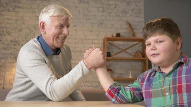 Großvater und Enkel ringen zu Hause in einem gemütlichen Zimmer um den Arm. Kräfte messen beim Armdrücken. alter Mann gewann. Wohnkomfort, Familienidylle, Gemütlichkeitskonzept, Generationenunterschied, hautnah. 60 fps — Stockvideo