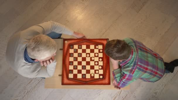 Abuelo y nieto juegan al ajedrez. El anciano enseña ajedrez para jugar a un niño gordo. Confort del hogar, idilio familiar, concepto de comodidad, diferencia de generaciones, tiro superior. 60 fps — Vídeos de Stock