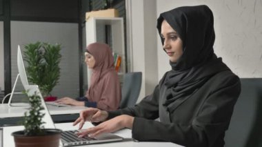 İki Müslüman kız ofiste, hijabs çalışmalarında yazın klavye, ekrana bakmak ve fotoğraf makinesi vasıl belgili tanımlık son bak. Office, iş, iş, kadın, kavram. 60 fps