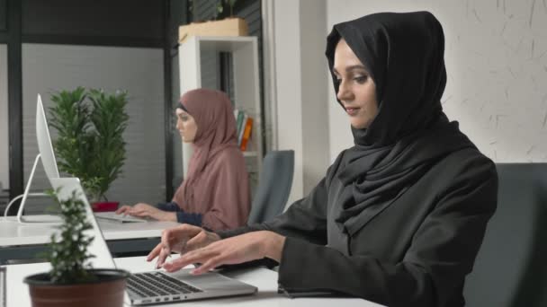 İki Müslüman kız ofiste, hijabs çalışmalarında yazın klavye, ekrana bakmak ve fotoğraf makinesi vasıl belgili tanımlık son bak. Odak çekme. Office, iş, iş, kadın, kavram. 60 fps — Stok video