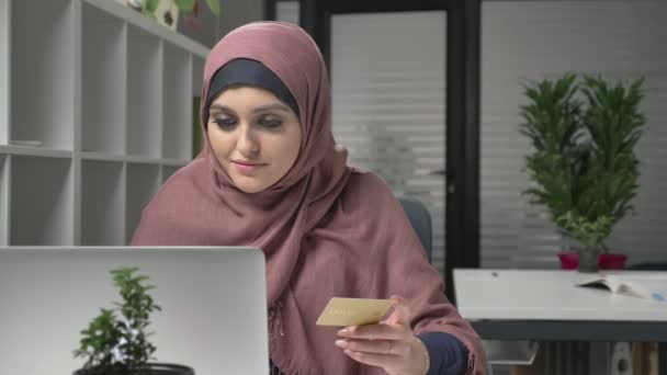 Joven chica hermosa en hijab rosa hace compras en Internet desde el ordenador portátil. Tarjeta de crédito. 60 fps — Vídeo de stock