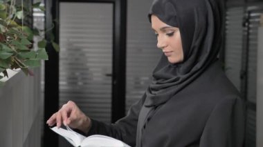 Siyah Tesettür güzel genç kızı ofiste anlamına gelir ve kitap okur. Kameraya benziyor 60 fps
