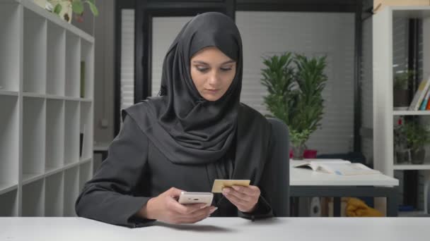 戴着黑色头巾的年轻漂亮女孩在互联网上购买智能手机。信用卡。60 fps — 图库视频影像