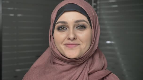 Ung vacker flicka i rosa hijab leende och tittar på kameran. Porträtt, närbild 60 fps — Stockvideo