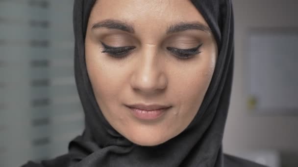 Молодая красивая девушка в черном хиджабе улыбается и смотрит в камеру. Портрет, около 60 кадров в секунду — стоковое видео
