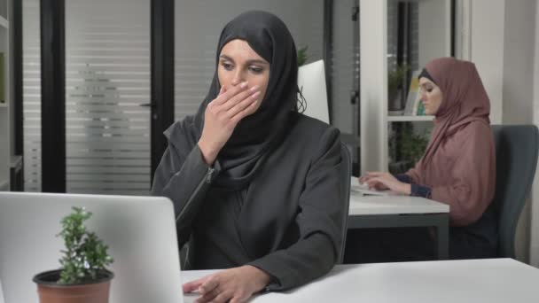 Flicka i svart hijab sitter i kontoret och hosta, en sjukdom, förkylning, en sjukdom är ett begrepp. Flicka i rosa hijab i bakgrunden. 60 fps — Stockvideo
