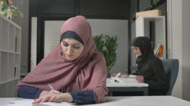 Genç güzel kız pembe bir hijab içinde bir defterde yazar öğrenir, çalışma. Arap kadınları ofiste 60 fps