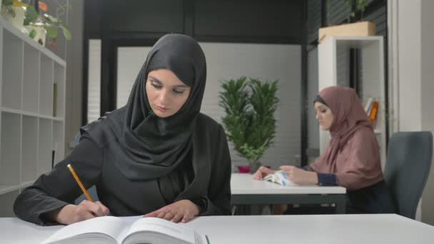 O tânără fată frumoasă într-un punct și un hijab negru va scrie în limba arabă. Femei arabe în birou 60 fps — Videoclip de stoc