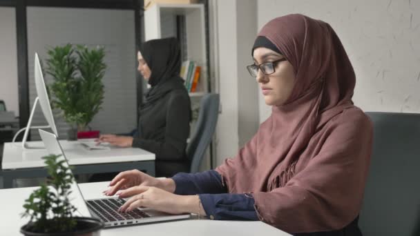 Dvě mladé krásné Arabské dívky ve hijabs práce v kanceláři, psaní. 60 snímků za sekundu — Stock video