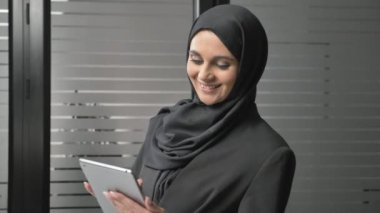 Siyah Tesettür içinde güzel bir genç kız bir tablet kullanır, Fotoğraflar, Resimler, gülümseyen görünüyor. Arap kadınları ofiste. 60 fps