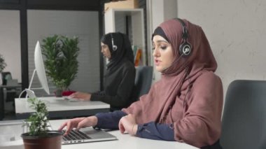 Pembe bir hijab bir genç güzel kız kulaklığı, çağrı merkezi Ýþlemi konuşuyor. Arap kadınları ofiste. 60 fps