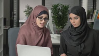 Hijabs iki güzel genç kız ofiste oturup tartışmak zamanlamaları, iş, diyalog, konuşma. 60 fps