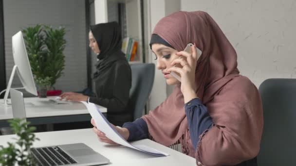 Fiatal lány gyönyörű pink hidzsáb, a dokumentumok, és beszél a mobiltelefon. Arab nők az irodában. 60 fps — Stock videók