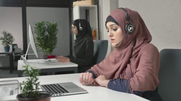 Pembe bir hijab bir genç güzel kız kulaklığı, çağrı merkezi Ýþlemi konuşuyor. Arap kadınları ofiste. 60 fps — Stok video