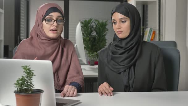 Две красивые девушки в хиджабах сидят в офисе и обсуждают расписание, бизнес, диалог, беседу. 60 кадров в секунду — стоковое видео