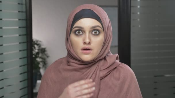 Uma jovem árabe em hijab vermelho é surpreendida, mostra uma emoção de surpresa. Olha para a câmara, retrato. 60 fps — Vídeo de Stock