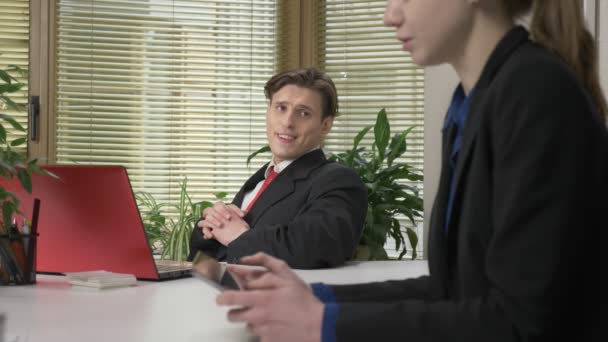 Mladý muž v obleku sedí v kanceláři, dialog a podřízená žena. Flirtovat s holkou. Práce v kanceláři. 60 snímků za sekundu — Stock video