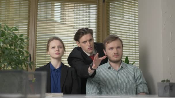 Young man in a suit makes a presentation to two employees of the office. He tells the story impulsively, gestures with his hands. Work in the office concept. 60 fps — Stock Video