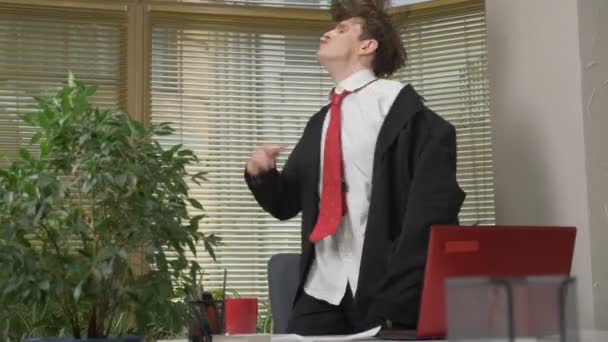 Joven en traje baila en la oficina, hace caras graciosas, tontos alrededor, se regocija. Trabajo en el concepto de oficina 60 fps — Vídeo de stock