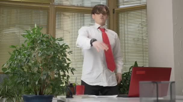 Ung man i en kostym danser på kontoret, gör roliga miner, lurar, jublar. Arbeta i office concept 60 fps — Stockvideo