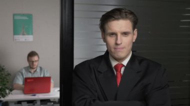 Takım elbiseli genç başarılı işadamı ofiste katlanmış ellerle duruyor. Kıç tarafa bak, ciddi. Adam içinde belgili tanımlık geçmiş bir bilgisayarda çalışıyor. 60 fps