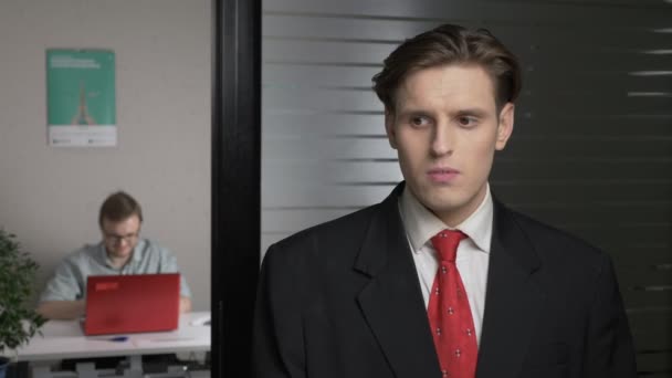 Ung forretningsmand i jakkesæt, der laver ansigtsløftning. Mennesket arbejder på en computer i baggrunden. 60 fps – Stock-video