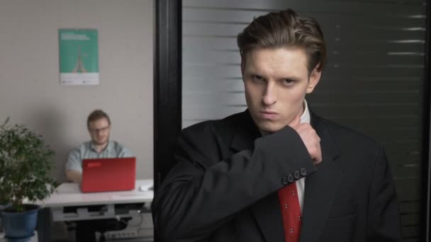 スーツの若いビジネスマンを脅かす、カメラで見えます。男は、バック グラウンドでコンピューターで動作します。60 fps — ストック動画