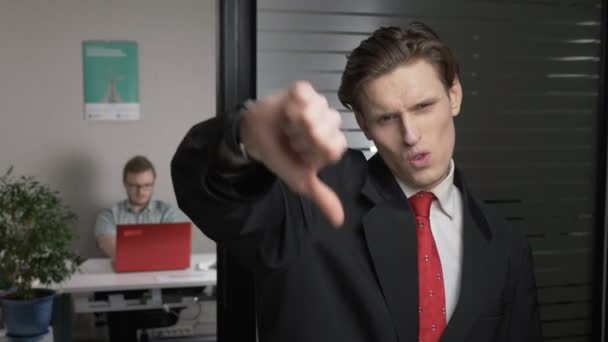 スーツの若いビジネスマンは、嫌いな兆候を示しています親指ダウン。男は、バック グラウンドでコンピューターで動作します。60 fps — ストック動画
