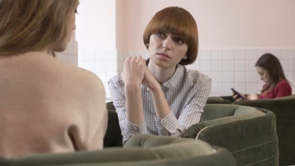 Tre giovani ragazze caucasiche sedute in un caffè e sorridenti, parlando, dialogando, emozione di tristezza, concetto di pettegolezzo. Sfondo 60 fps — Video Stock